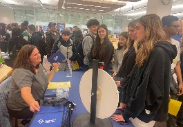four students stand and speak with business representative who is sitting behind a table 